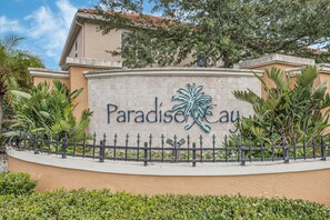 Ein Schild mit dem Schriftzug 'Paradise Cay', umgeben von einer Zierumzäunung und üppiger Vegetation.