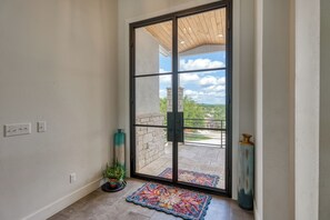 A room with a sliding glass door leading to a balcony, a potted plant, a rug, and a tall vase. - Amazing 4-bedroom House with Pool, Golf Simulator, and Batting Cage. (Lago Vista)
