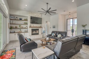 A modern living room with a fireplace, leather sofas, a coffee table, and a stone accent wall. - Amazing 4-bedroom House with Pool, Golf Simulator, and Batting Cage. (Lago Vista)