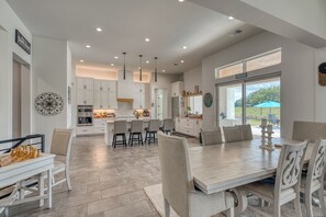 A spacious kitchen with white cabinetry, a central island, and a dining area with a large table and chairs. - Amazing 4-bedroom House with Pool, Golf Simulator, and Batting Cage. (Lago Vista)