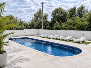 Ein rechteckiger Swimmingpool mit einer gefliesten Kante, umgeben von einer weißen Wand und einer Reihe weißer Liegestühle.