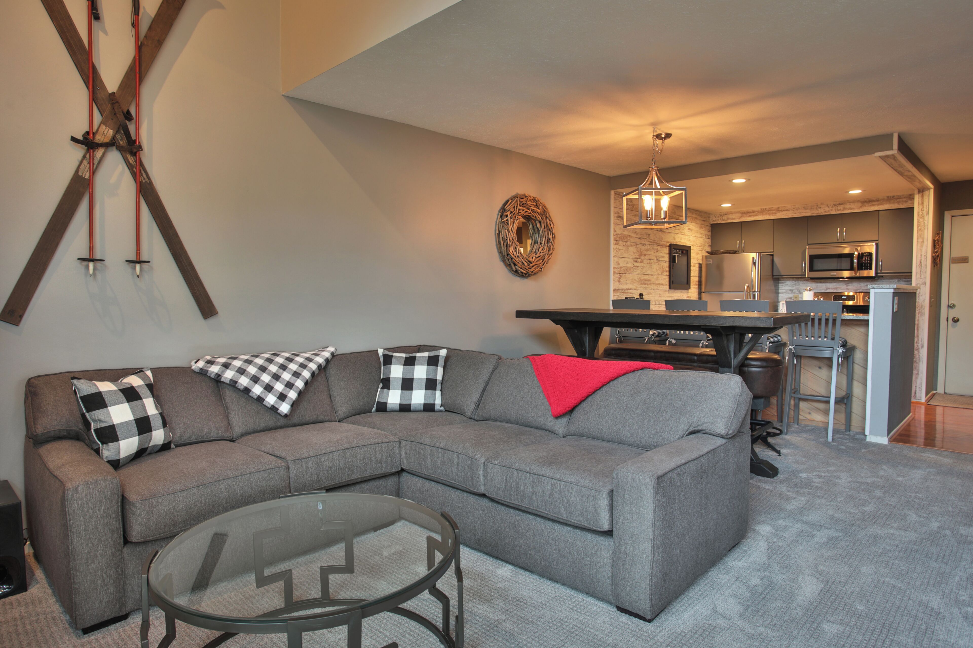 A living room with a sectional sofa, a glass coffee table, and a kitchen in the background.
