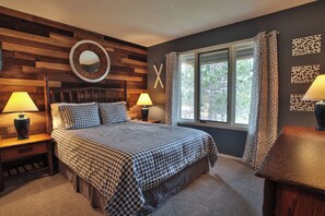 A bedroom with a wooden headboard, a large bed with checkered bedding, two bedside lamps, a window with patterned curtains, and a wall-mounted mirror. - Spacious 3 bdrm, 2 Bath Plus Loft, 1630 Sq Ft.  Many onsite amenities with Golf/Skiing near by! (Harbor Springs)
