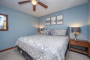 A bedroom with a bed, a nightstand, a lamp, a ceiling fan, and wall art.