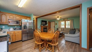 A kitchen with wooden cabinets, a microwave, a refrigerator, and a dining table with chairs. - New! Lake Area Chalet w/ Hot Tub (Swanton)