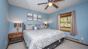 A bedroom with a bed, nightstands, a ceiling fan, a window with curtains, and wall art. - New! Lake Area Chalet w/ Hot Tub (Swanton)