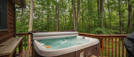 A hot tub on a wooden deck surrounded by a forest.