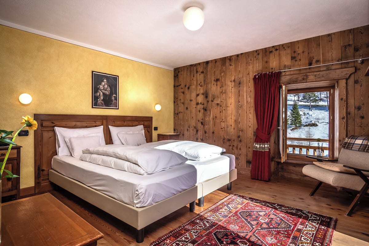 A wooden-paneled room with a bed, a chair, a window with a view of snow, and a wall-mounted picture.