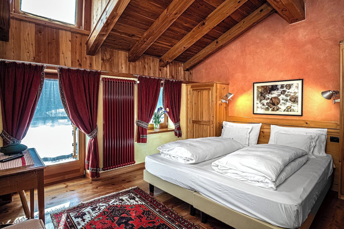 A wooden room with a bed, curtains, a desk, and a window.
