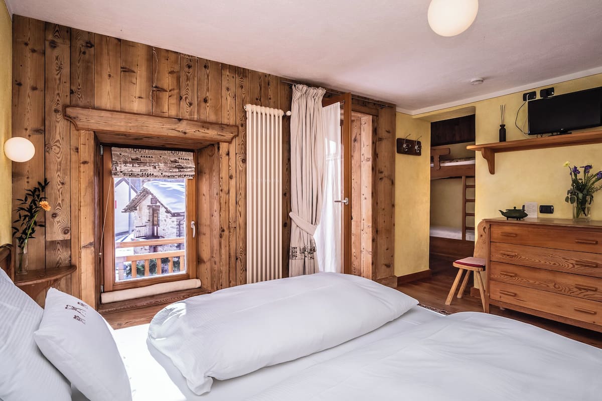 A wooden-paneled room with a bed, a dresser, a TV, and a window with curtains.