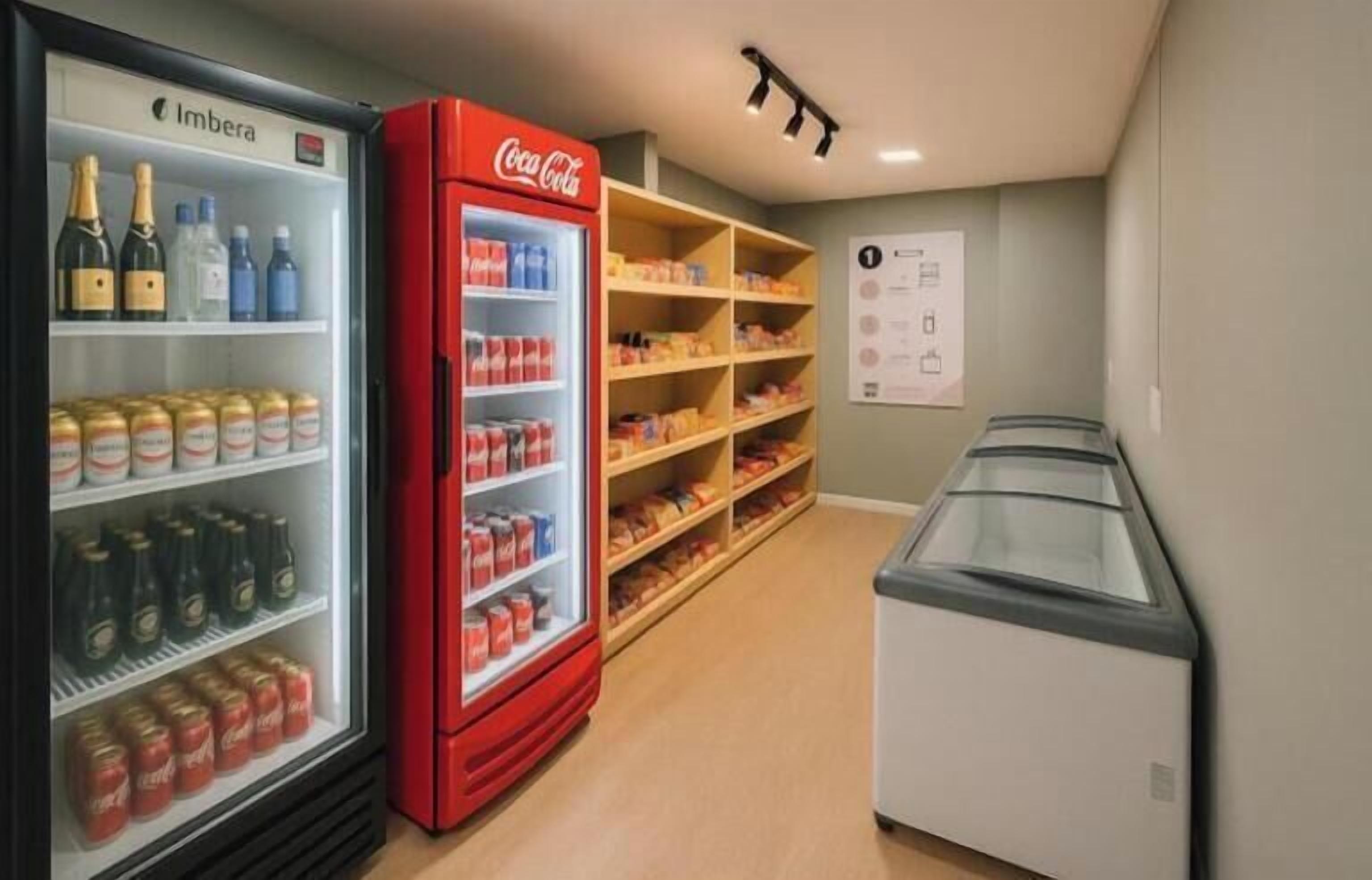 A hotel room with a minibar, a refrigerator with Coca-Cola and Imbéras, and shelves with snacks.