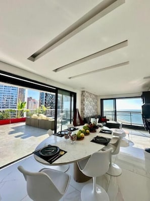 Uma área de jantar moderna com uma mesa redonda, cadeiras brancas e vista para o oceano.