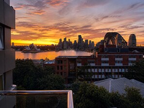 A city skyline at sunset with a prominent bridge and the Sydney Opera House. - Iconic Harbour Views & Free Parking (Kirribilli)