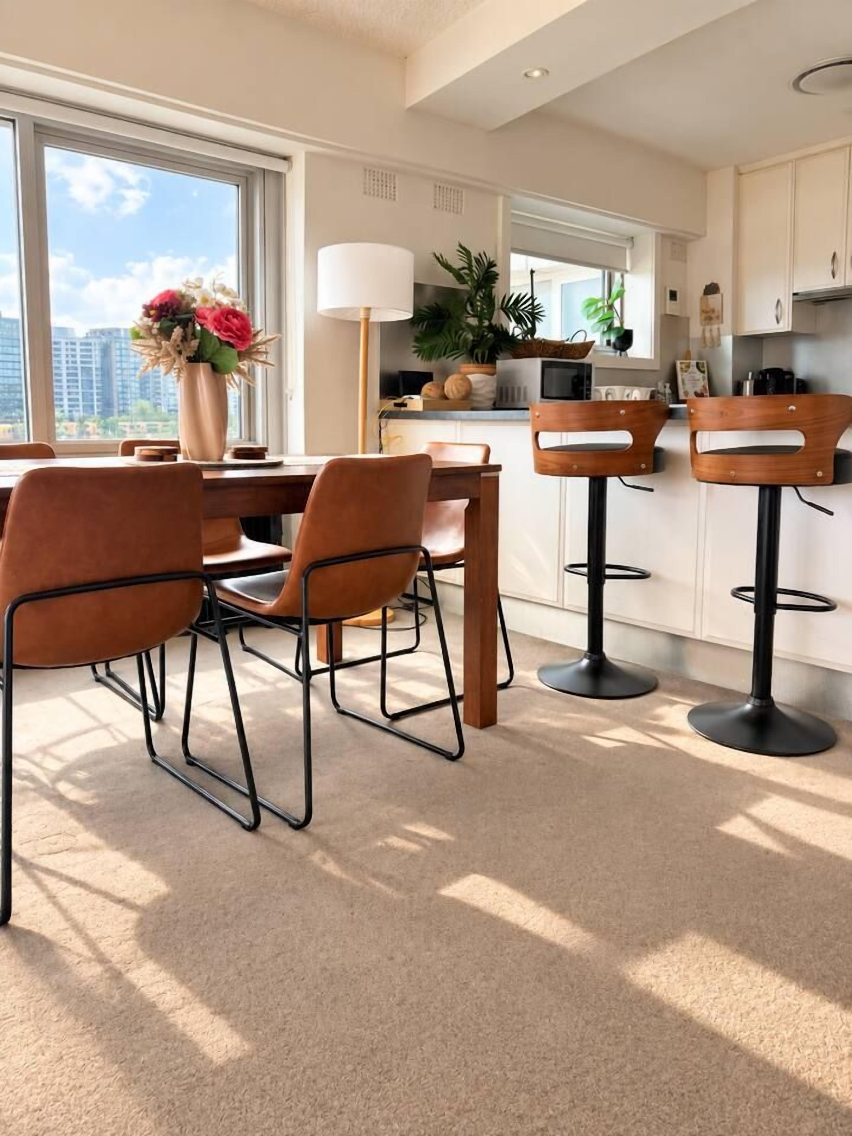 A modern kitchen with a dining area, featuring a large window, a vase with flowers, and a bar stool.