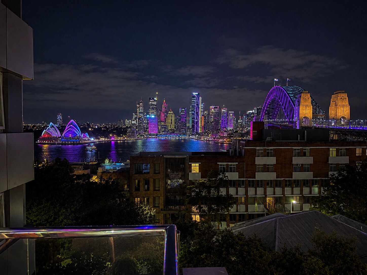 A nighttime cityscape with illuminated buildings and a bridge.
