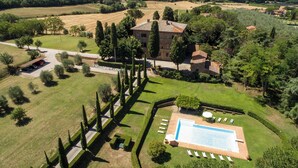 Eine Vogelperspektive zeigt eine Villa mit Swimmingpool, umgeben von gepflegten Gärten und einer ländlichen Gegend.