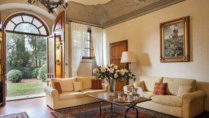 Ein Wohnzimmer mit zwei Sofas, einem Couchtisch, einer Vase mit Blumen, einem Gemälde an der Wand und Blick ins Freie.