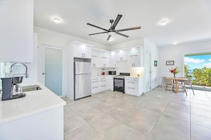 Una cocina moderna con muebles blancos, un refrigerador de acero inoxidable, una estufa a gas y un ventilador de techo.