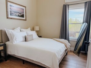A neatly made bed with white bedding, a bedside lamp, a framed picture on the wall, and a window with curtains. - Cozy Modern Retreat in Floyd with Fire Pit and Peaceful Mountain Views (Floyd)