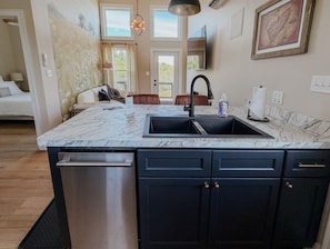 A kitchen with a marble countertop, black cabinets, and a stainless steel dishwasher. - Cozy Modern Retreat in Floyd with Fire Pit and Peaceful Mountain Views (Floyd)