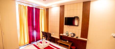 A hotel room with a bed, a desk, a television, and a window with curtains.