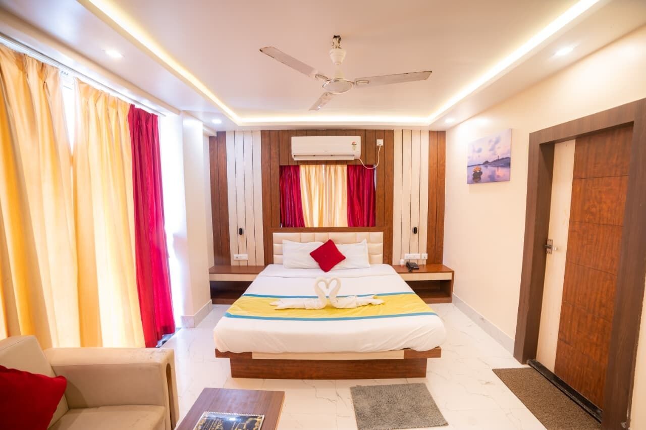 A hotel room with a bed, a ceiling fan, an air conditioning unit, a nightstand, a chair, and a door.
