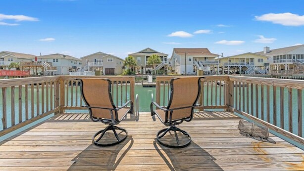 A wooden deck with two chairs facing a marina, overlooking houses and a clear sky. - Silver Sand Dollar - Channel House - Firepit (North Myrtle Beach)