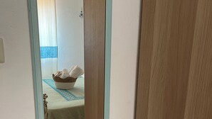 Ein Zimmer mit einem Bett, einem Tisch mit blauer Tischdecke und einem Spiegel, der das Zimmer widerspiegelt.