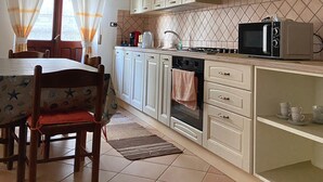 Eine Küche mit weißen Schränken, einer Mikrowelle, einem Backofen und einem Esstisch mit Stühlen.