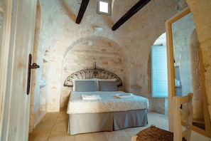 Un dormitorio con pared de piedra, una cama con cabecera, una ventana y una puerta.