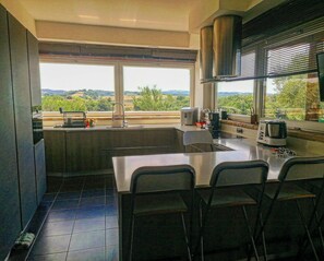 Una cuina moderna amb una finestra gran, un rentapeus, una cuina i una zona de dinar amb cadires.