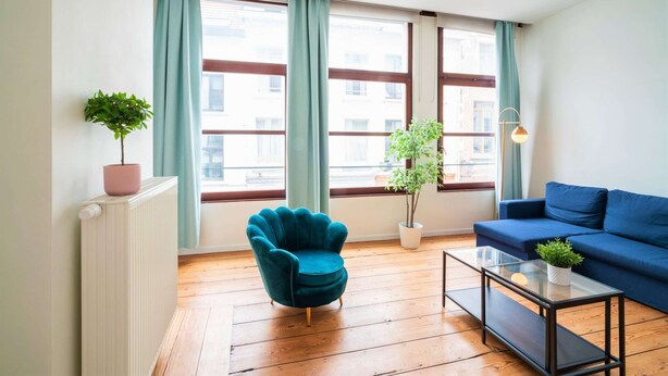 Una sala de estar con un sofá azul, un sillón verde azulado, una mesa de centro de vidrio y una planta en maceta.