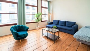 Una habitación con un sillón azul, un sofá, una mesita y una planta en maceta.