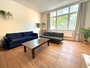 Una sala de estar con dos sofás, una mesa de centro y un ventanal con cortinas.