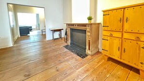 Ein geräumiger Raum mit Holzboden, Kamin, einem kleinen Tisch und einem gelben Schrank.