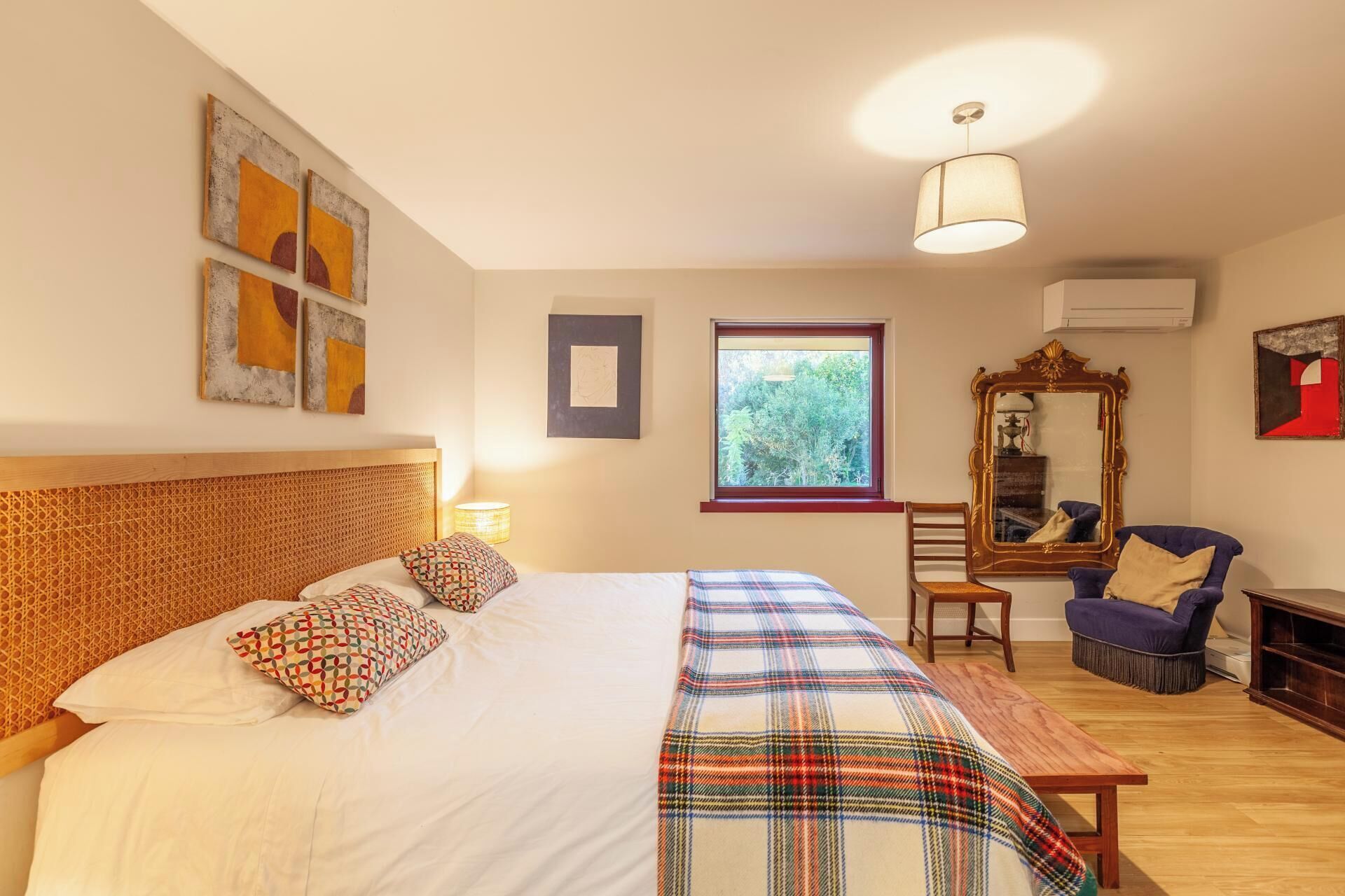A bedroom with a bed, a wooden headboard, a window, a mirror, a chair, and a table.