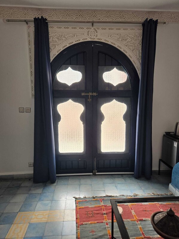 A room with a large arched door with intricate designs, a patterned rug on the floor, and a small table with a decorative item. - VILLA LATIFA Room in Agadir (Ghazoua)