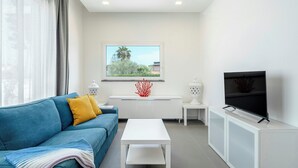A modern living room with a blue sofa, white coffee table, and a TV on a white cabinet. - Modern villa with pool in Fontane Bianche (Siracusa)