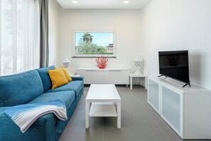 A modern living room with a blue sofa, white coffee table, and a TV on a white cabinet. - Modern villa with pool in Fontane Bianche (Siracusa)