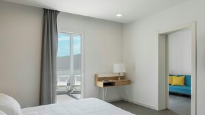 A hotel room with a bed, a desk with a lamp, a view of a balcony, and a sofa in the adjacent room. - Modern villa with pool in Fontane Bianche (Siracusa)
