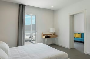 A hotel room with a bed, a desk with a lamp, a view of a balcony, and a sofa in the adjacent room. - Modern villa with pool in Fontane Bianche (Siracusa)