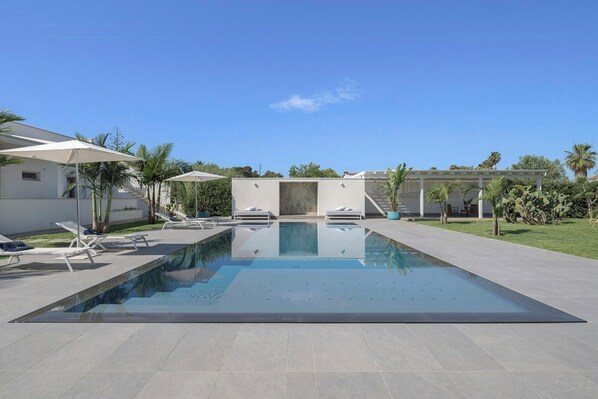 Piscina retangular com superfície de água azul cristalina, rodeada por um deck ladrilhado.