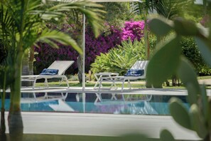 Área da piscina com espreguiçadeiras e reflexo do verde ao redor.