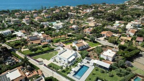 An aerial view of a residential area with houses, a swimming pool, and a clear view of the sea. - Modern villa with pool in Fontane Bianche (Siracusa)