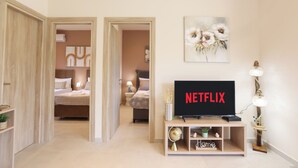 Moderni hotellihuone, jossa on televisio, jolta näkyy Netflix, sänky, yöpöytä, lamppu ja seinälle ripustettu taideteos.