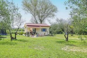 Ein kleines Haus mit rotem Dach, umgeben von einem grünen Rasen und Bäumen.