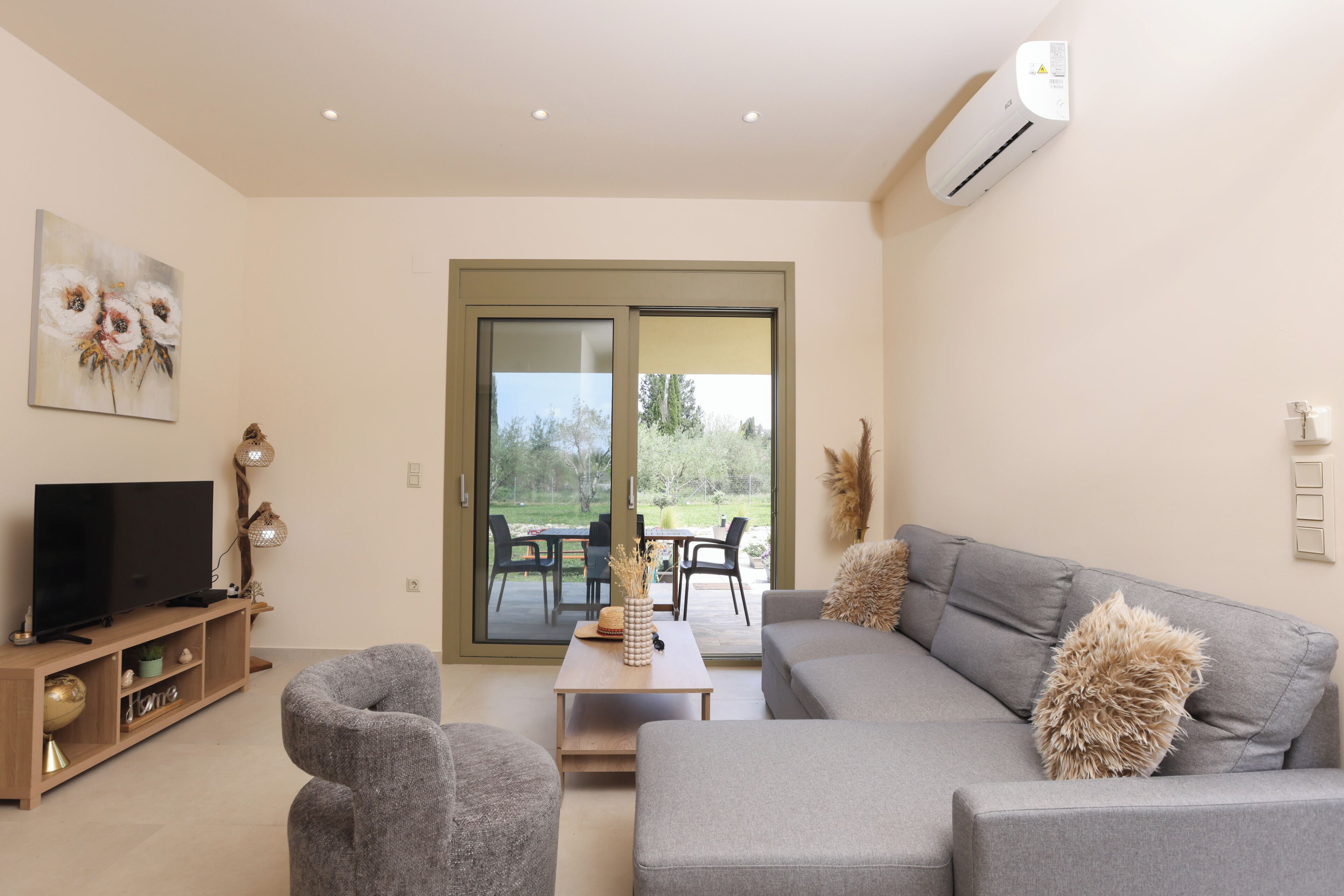 Una sala de estar moderna con un sofá gris, un televisor sobre un mueble de madera y un ventanal corredero que da a un patio exterior.