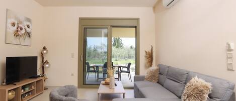 A modern living room with a grey sofa, a television on a wooden stand, and a sliding glass door leading to an outdoor patio.