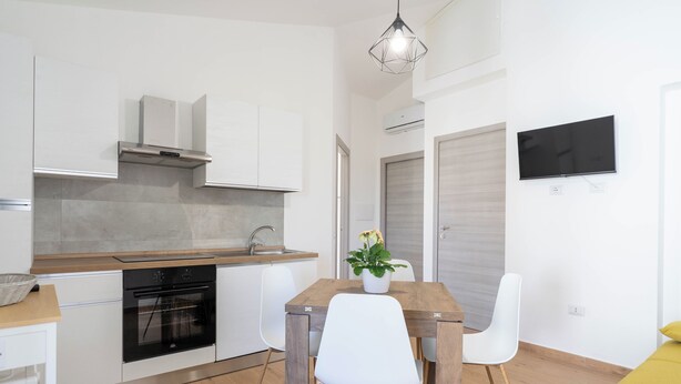 Una cocina moderna con armarios blancos, horno integrado y una zona de comedor con mesa de madera y sillas blancas.