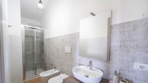 Un baño moderno con ducha envuelta en vidrio, un lavabo blanco y un mueble de tocador de madera.